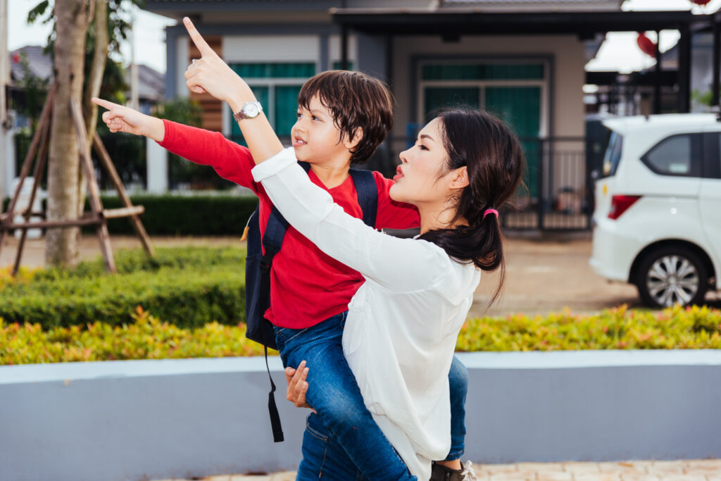 appy mother carrying and walking her kid, the kid point hand finger out outdoors, Back to home from school concept